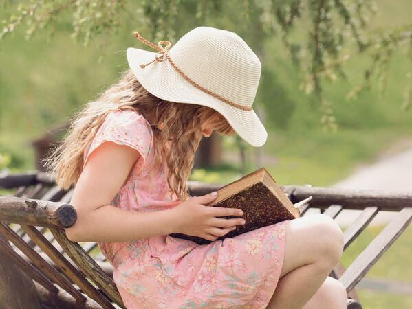 Foto von einem Mädchen mit Sonnenhut, das ein Buch liest
