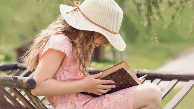 Foto von einem Mädchen mit Sonnenhut, das ein Buch liest